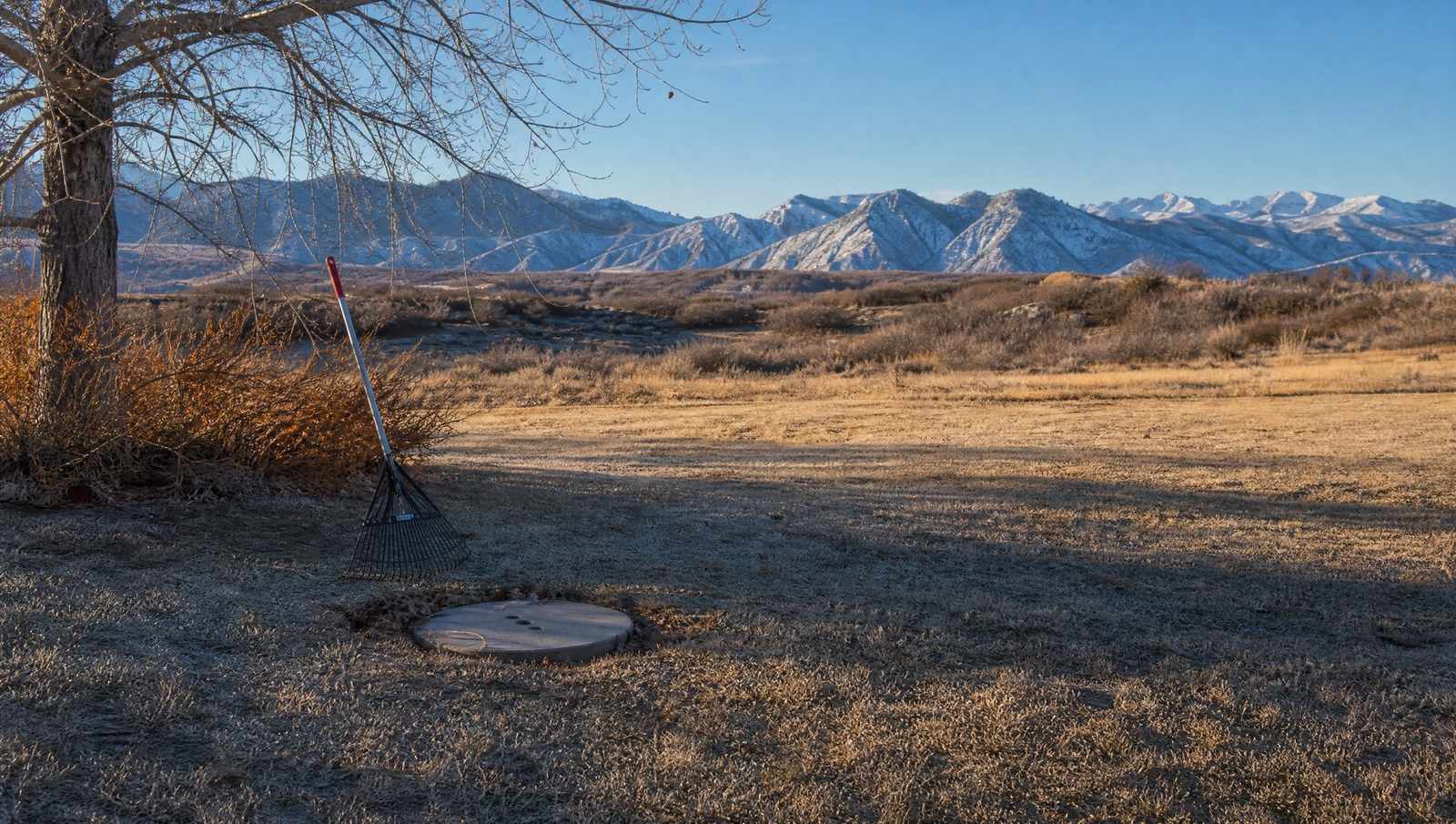 Frosted late fall Colorado yard with a septic access lid cleared of leaves and early snow on the foothills