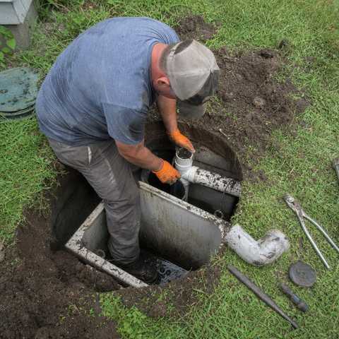 Technician replacing a septic tank baffle and outlet pipe in an excavated yard